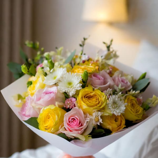 Bouquet of pink and yellow roses with white daisies wrapped in white paper