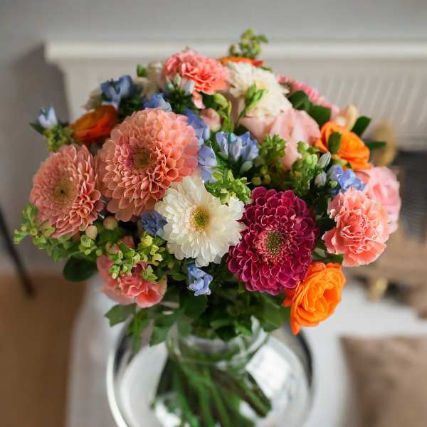 Mixed bouquet of pink, white, blue, and orange flowers in a glass vase