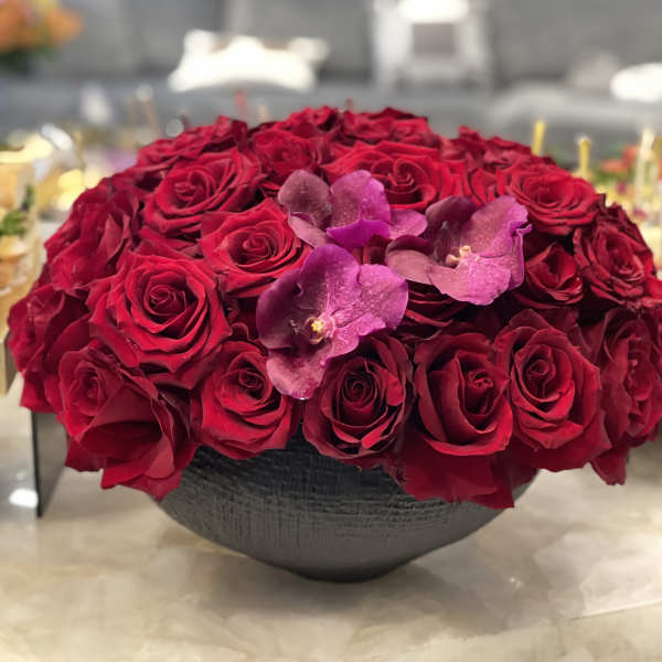 Red rose arrangement with purple orchids in a dark bowl vase