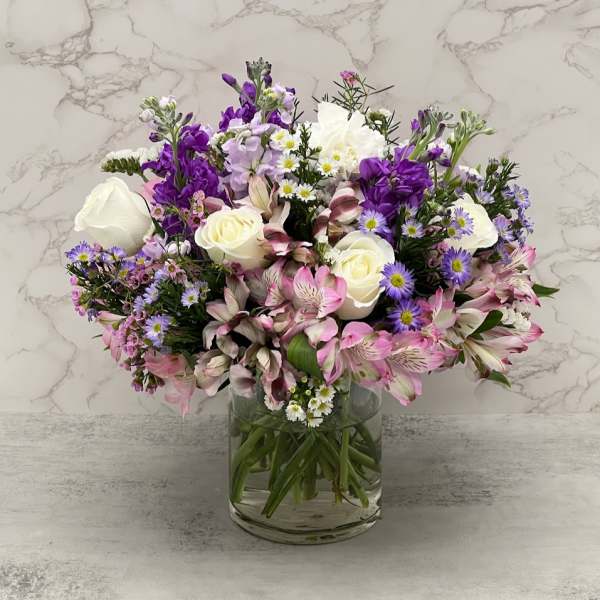 Mixed bouquet of white roses, purple blooms, and pink flowers in a glass vase