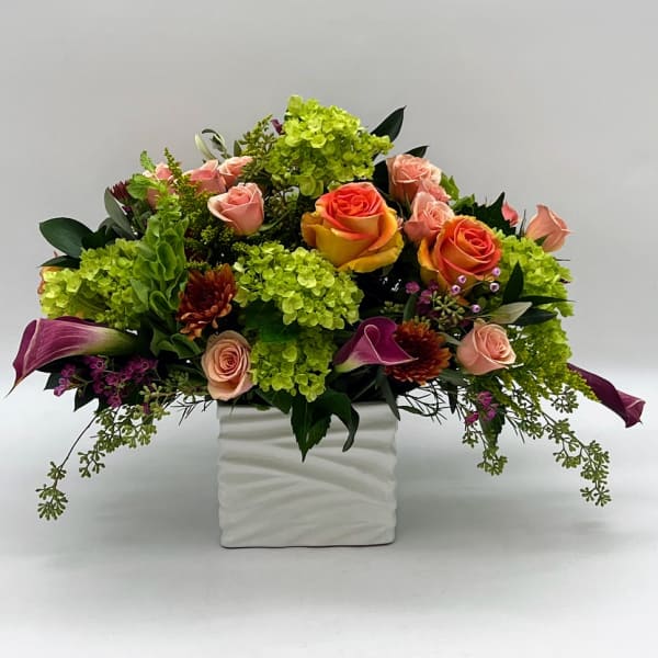 Mixed floral arrangement in a white square vase with pink and orange roses