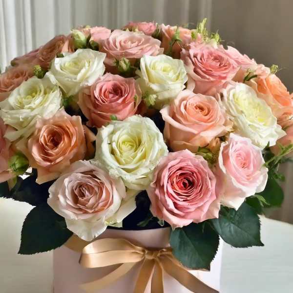 Pink and white roses arranged in a round hatbox with a ribbon