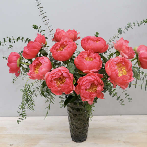 Tall arrangement of bright pink peonies with trailing eucalyptus in a textured glass vase