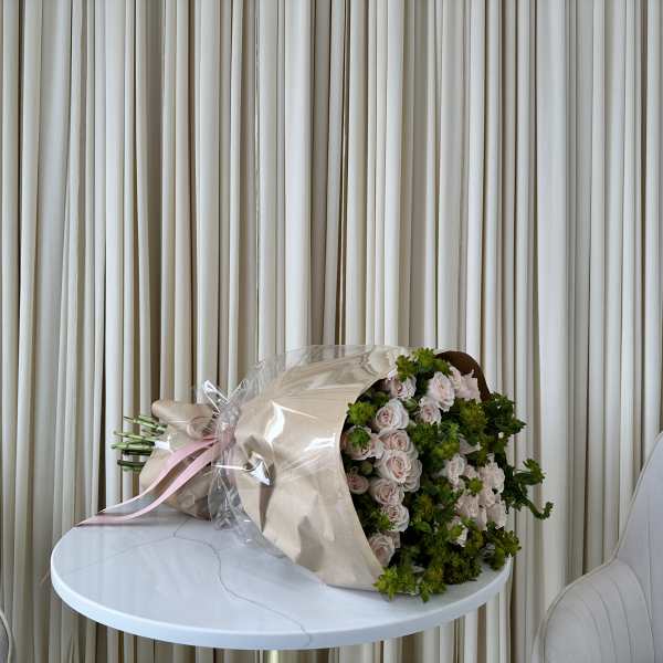 Bouquet of pale pink roses wrapped in beige paper with a pink ribbon