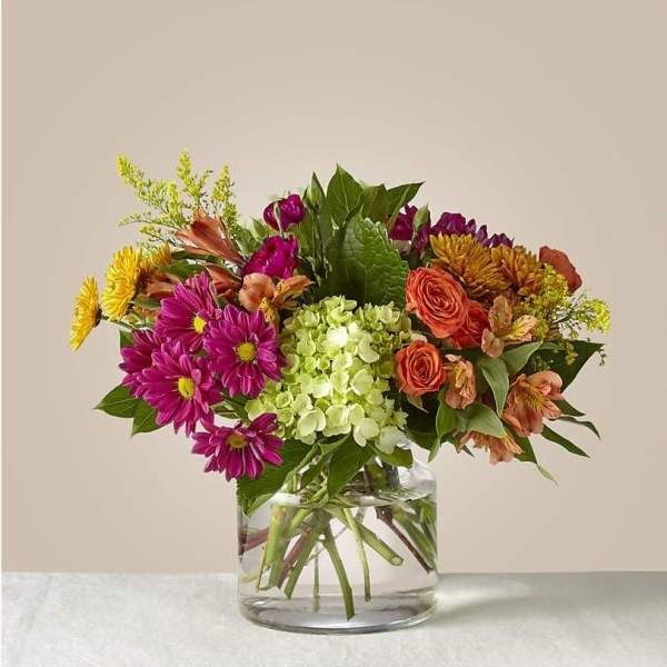 Mixed bouquet of purple, orange, and yellow flowers in a clear glass vase