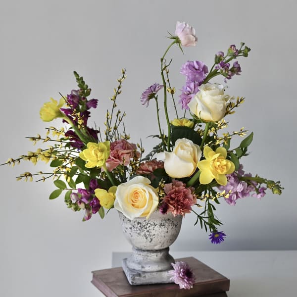 Mixed bouquet of roses, tulips, and purple blooms in a gray pedestal vase