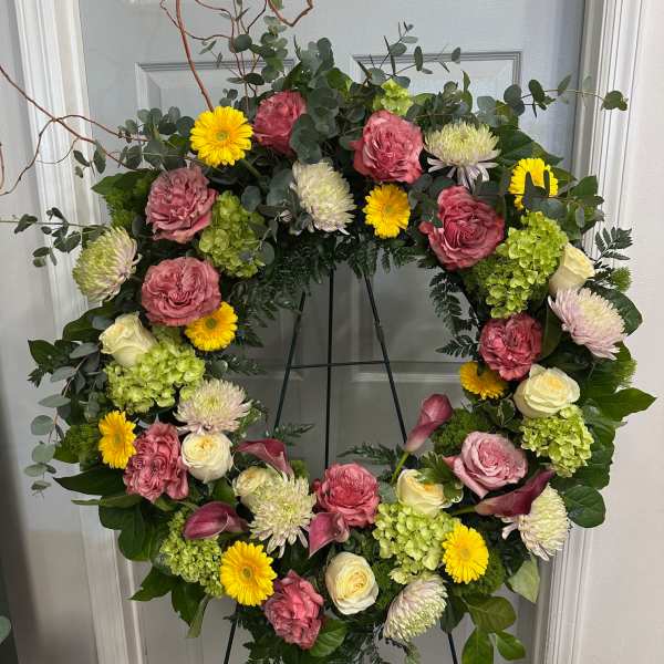 Large floral wreath with pink roses, yellow daisies, and green hydrangeas on an easel