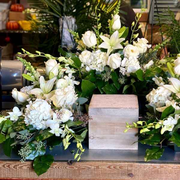 White floral arrangement with lilies and roses around a wooden cube