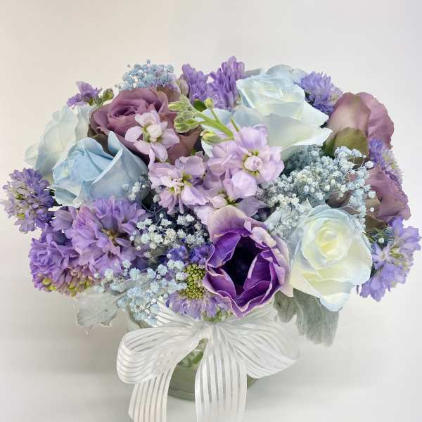Bouquet of pastel purple, blue, and white flowers in a glass vase with a white ribbon