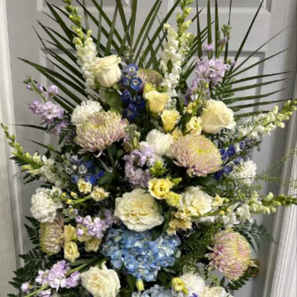 Tall standing floral spray with blue hydrangeas, white roses, and pastel blooms