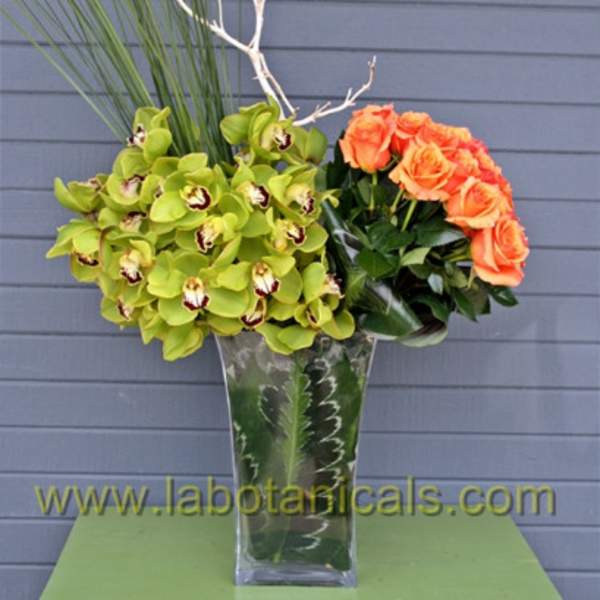 Orange roses and green orchids in a tall glass vase