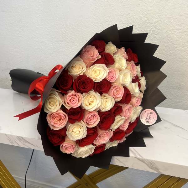 Bouquet of red, pink, and white roses wrapped in black paper with a red ribbon