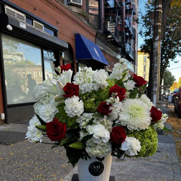 Red roses and white flowers arranged in a white bucket on a stand