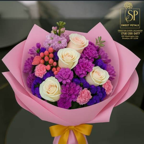 Pink-wrapped bouquet of cream roses, purple blooms, and pink accents with a yellow ribbon