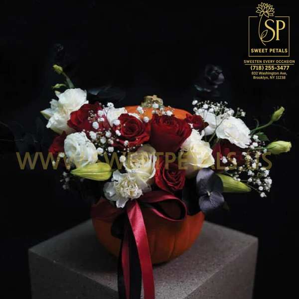 Red and white rose arrangement in an orange pumpkin vase with ribbon