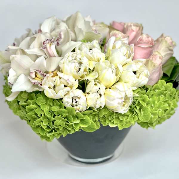 White orchids and pale pink roses in a dark vase with bright green hydrangeas