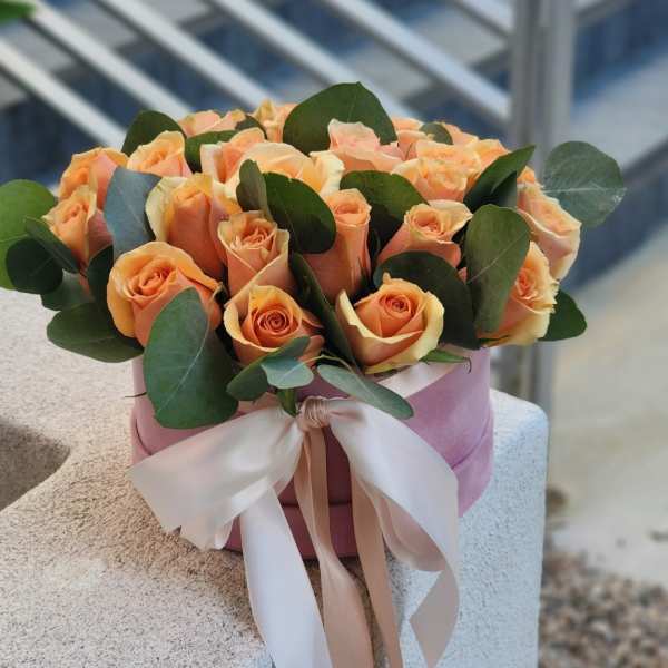 Peach roses arranged in a pink hat box with a ribbon bow