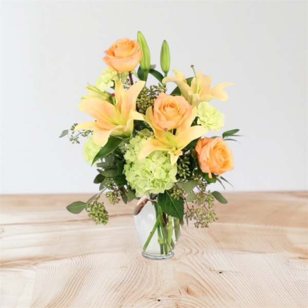 Peach roses and pale lilies in a clear glass vase
