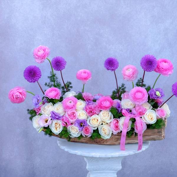 Pink and white flower arrangement in a wooden container with purple blooms