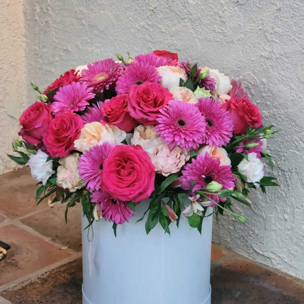 Pink roses and gerbera daisies arranged in a white hat box
