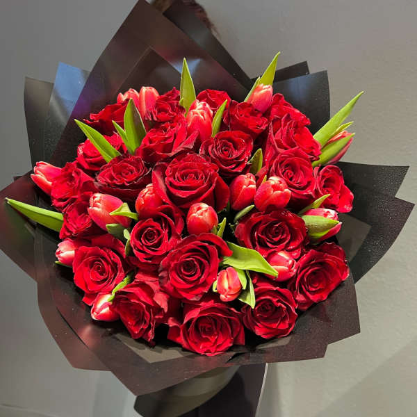 Bouquet of red roses and pink tulips wrapped in black paper