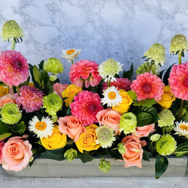 Rectangular floral arrangement with pink, yellow, and green blooms in a low container