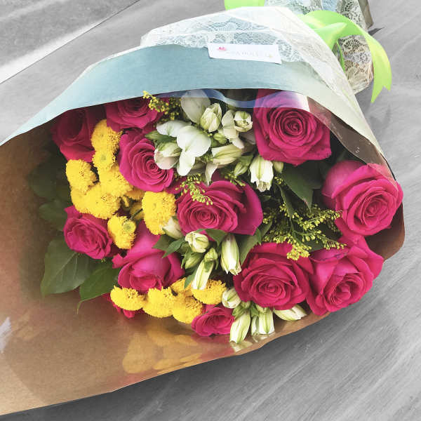 Bouquet of pink roses, white alstroemeria, and yellow pom flowers wrapped in pastel paper