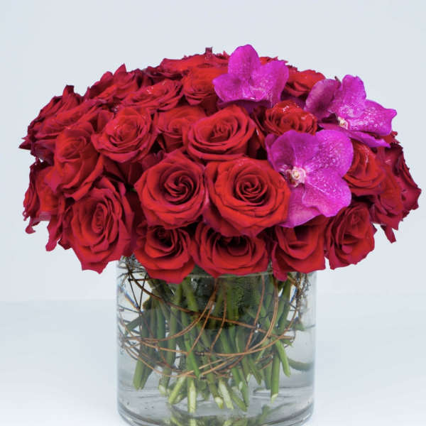 Red roses with purple orchids in a clear glass vase