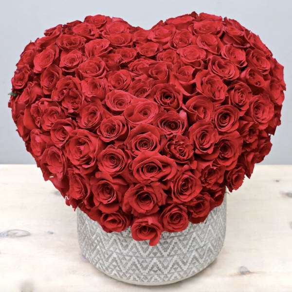 Heart-shaped arrangement of red roses in a patterned round container