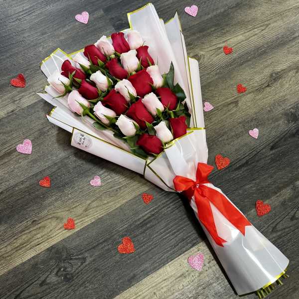 Bouquet of red and pale pink roses wrapped in white paper with a red ribbon