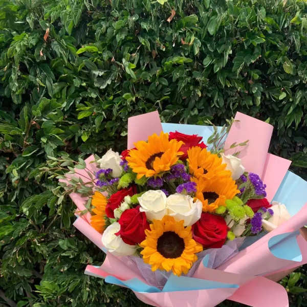 Bouquet of sunflowers, red and white roses, and purple filler flowers wrapped in pink paper