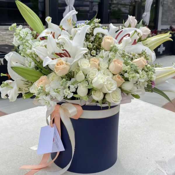 White lilies and pale roses arranged in a navy hatbox
