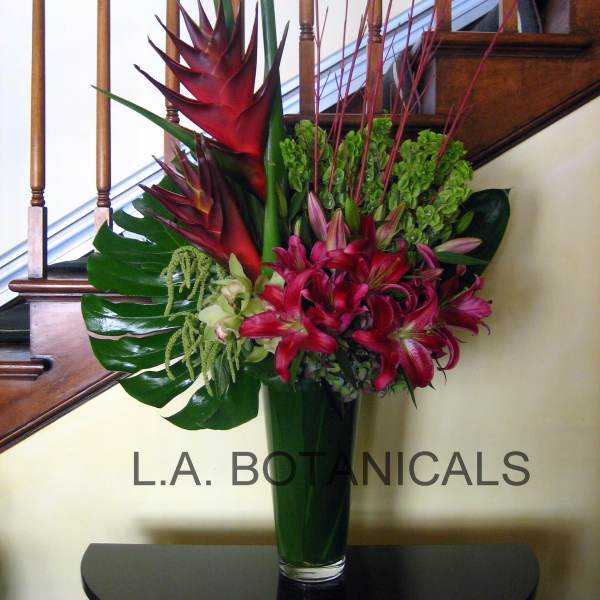 Tropical flower arrangement in a tall glass vase with red lilies and green foliage