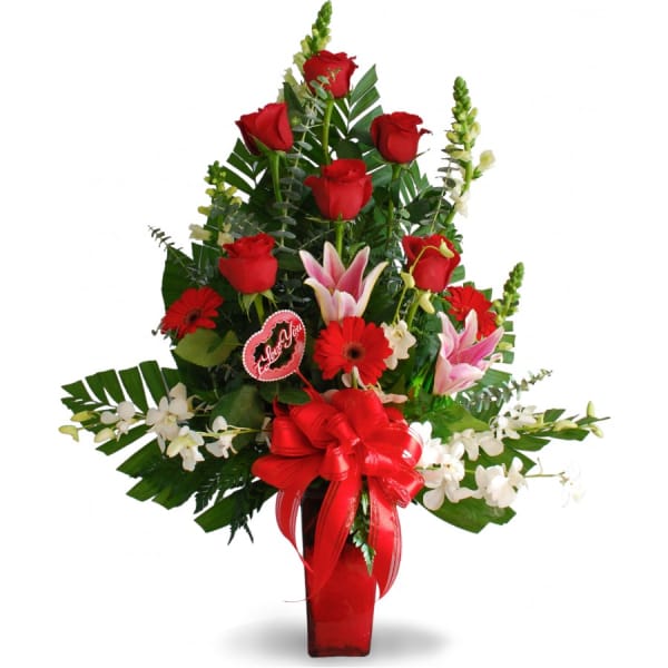 Red roses and lilies arranged in a tall red vase with a ribbon.