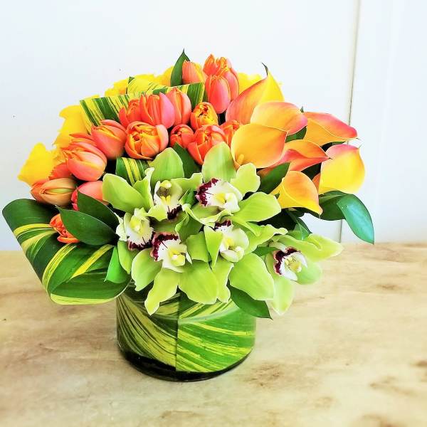 Bouquet of orange tulips and green orchids in a striped vase