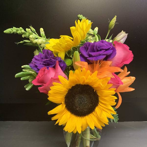Bright mixed bouquet with sunflowers, roses, and lilies in a glass vase