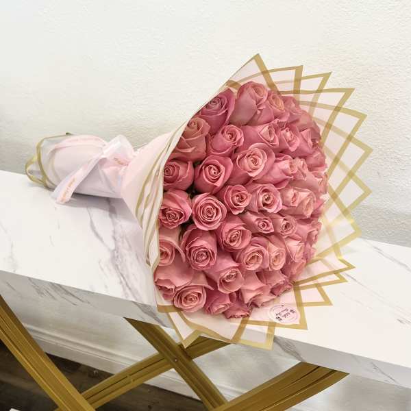 Bouquet of pink roses wrapped in pale paper with gold trim