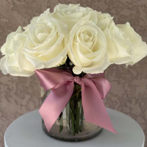 White rose bouquet in a glass vase with a pink ribbon