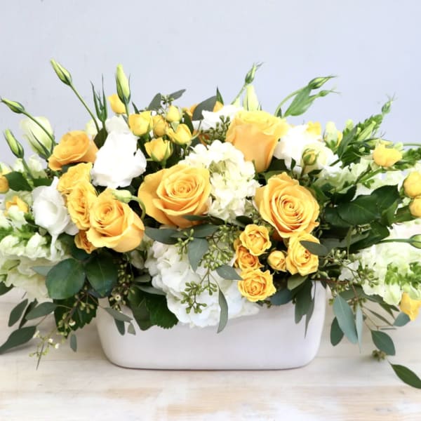 Yellow and white rose arrangement in a white rectangular vase