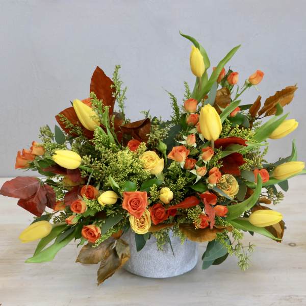 Low arrangement of yellow tulips and orange roses in a round white container