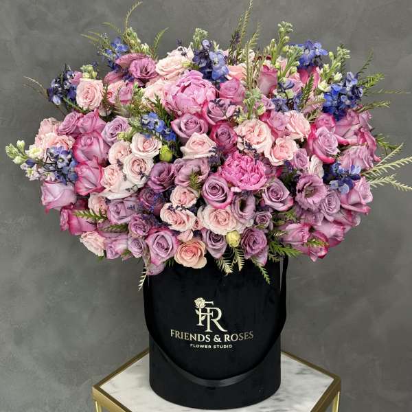 Large bouquet of pink and lavender roses with blue flowers in a black hat box