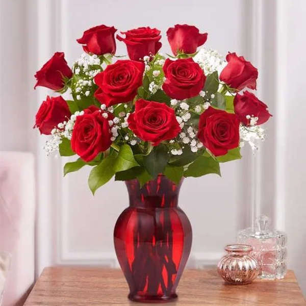 Red roses arranged in a red glass vase with white filler flowers