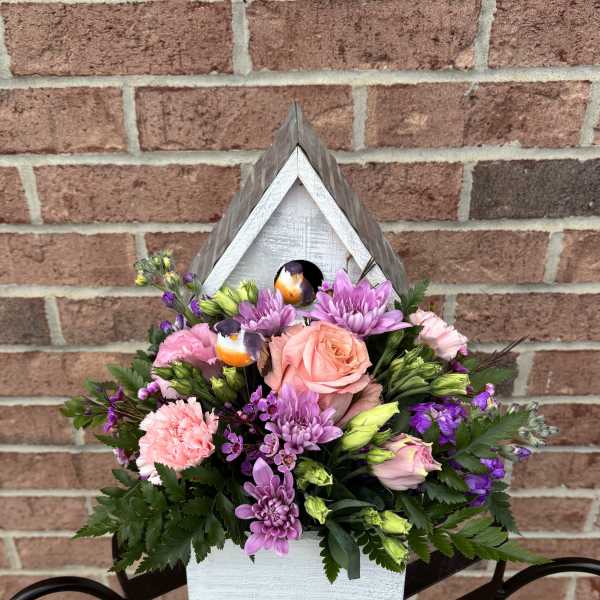 Mixed pink and purple flowers arranged in a white wooden birdhouse planter