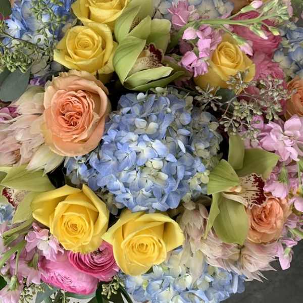 Colorful bouquet with blue hydrangeas, yellow roses, green orchids, and mixed pink and peach blooms