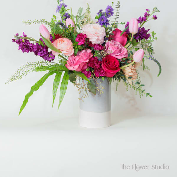 Asymmetrical pink and purple flower arrangement with tulips and roses in a tall white and gray cylinder vase