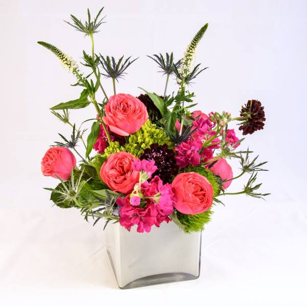 Pink roses and magenta flowers in a clear square vase