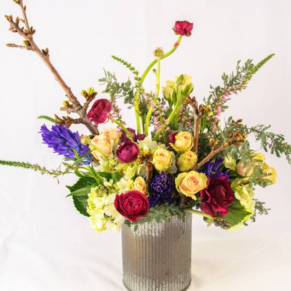 Mixed bouquet of roses, ranunculus, and hyacinth in a ribbed metal vase