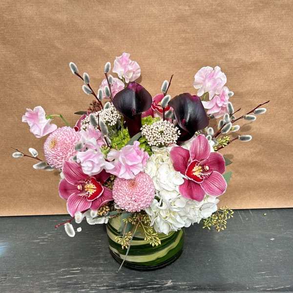 Pink and white floral arrangement with dark calla lilies in a green glass vase
