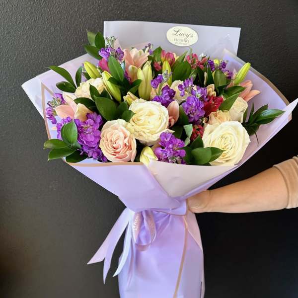 Bouquet of cream, blush, and purple flowers wrapped in lavender paper