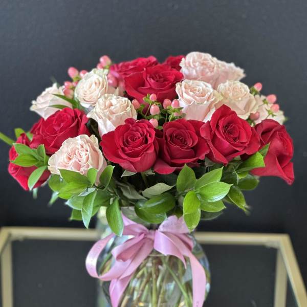 Bouquet of red and pale pink roses in a glass vase with a pink ribbon